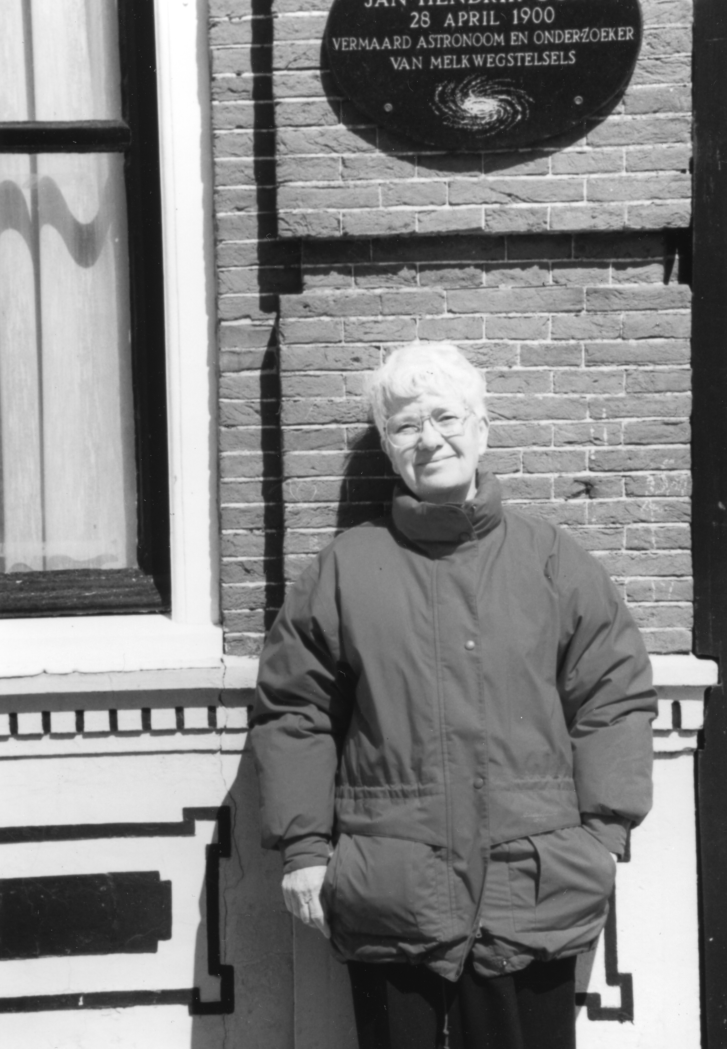 Photograph of Vera Rubin standing in front of Jan Oort's birthplace in Franeker, Netherlands. Rubin was Oort visiting professor at Leiden. Image information: Rubin Vera B2, AIP Emilio Segrè Visual Archives, Rubin Collection