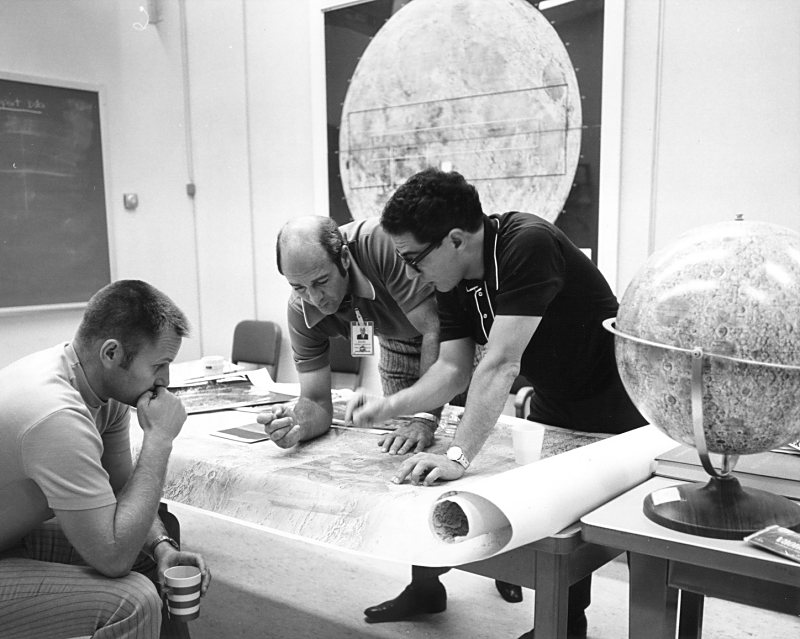 Farouk El-Baz reviewing lunar maps on a table with astronauts Ronald Evans and Robert Overmyer.