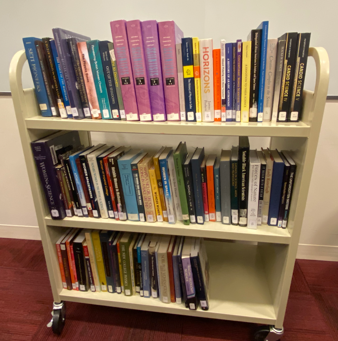 A three tiered bookshelf with multicolored books on each level.
