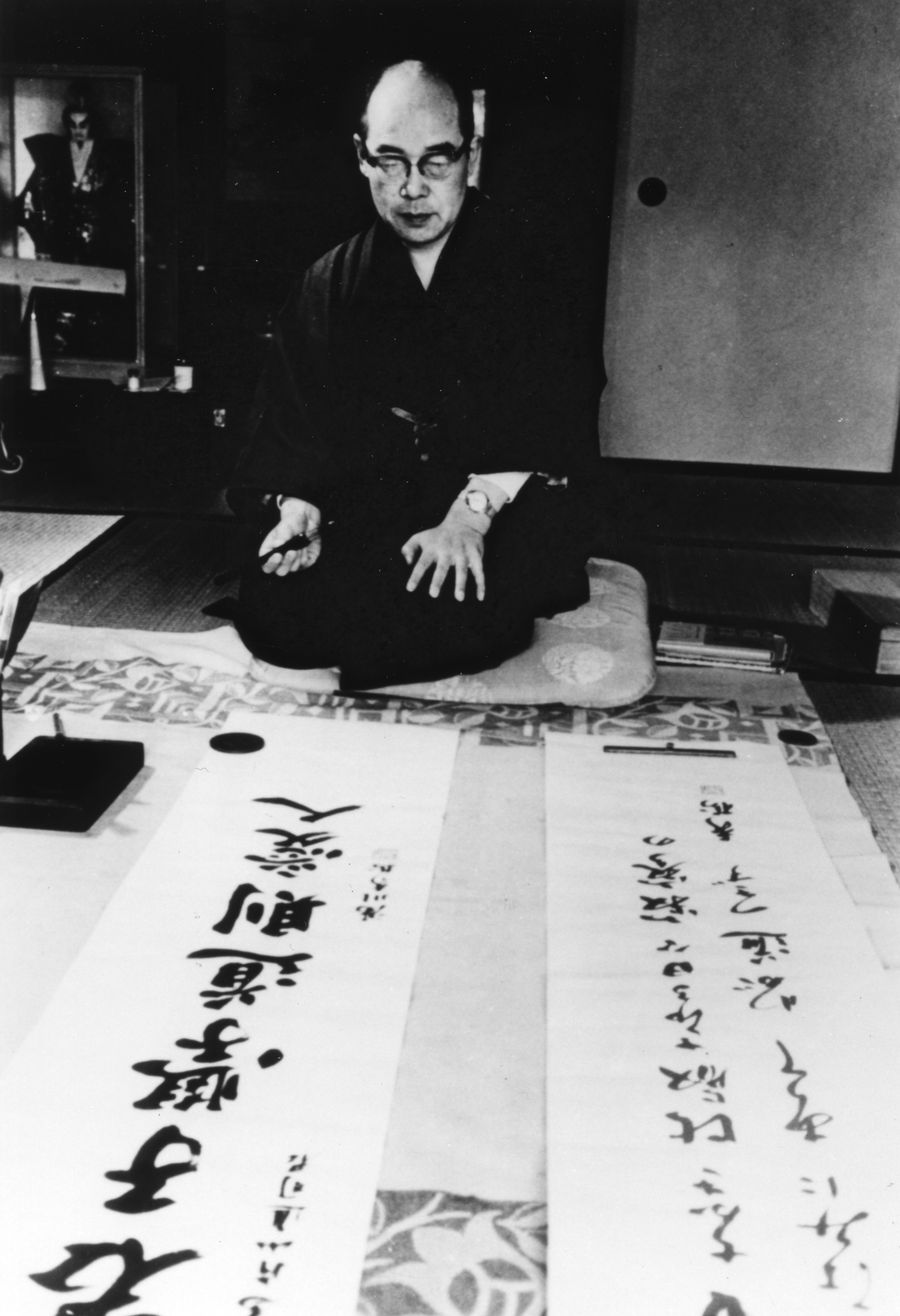 Hideki Yukawa sits on the floor with a brush in hand and pieces of calligraphy on the floor