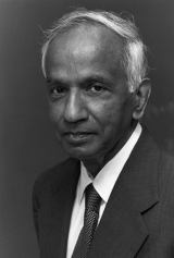 Portrait of S. Chandrasekhar. Black and white image. He is an older man in a suit and tie. He has kind eyes and very white hair.
