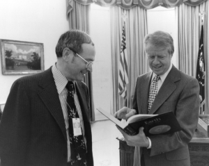 Frank Press looks on as President Jimmy Carter flips through Press's textbook