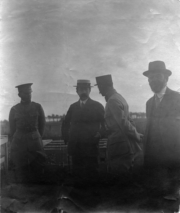a very hazy black and white photograph with four men standing outdoors, likely near the front. a line of trees and hills is just visible in the background. Leonard Loeb wears a U.S. army uniform, Rene Gosse is wearing a French military uniform, and the other two are in civilian clothing