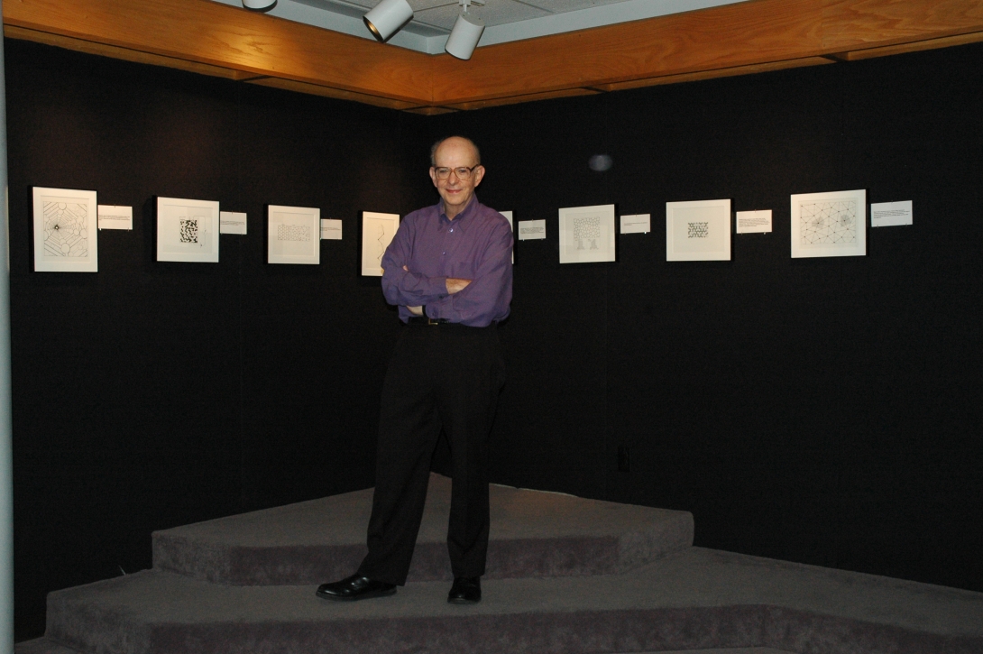 Professor Richard Zallen at the center of the photo in front of a 'art show' of physics-as-art at Wallace Hall, Virginia Tech, with seven images posted on a dark background