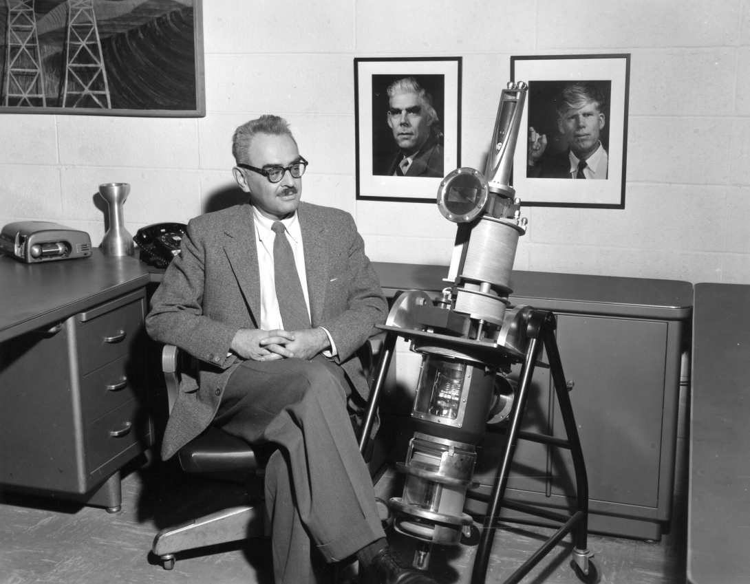 Marvin Chodorow, in his office, sits next to a person-sized model klystron. The model is basically rocket shaped; cylinders with a cone at the top.