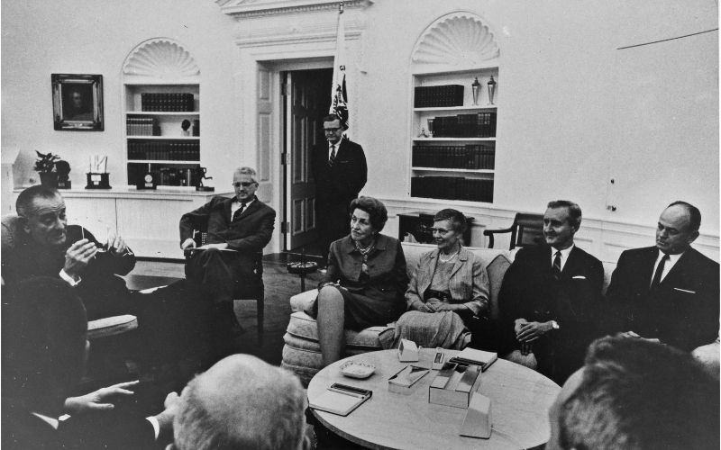 A group of people including Charlotte Moore Sitterly sit with President Johnson. 