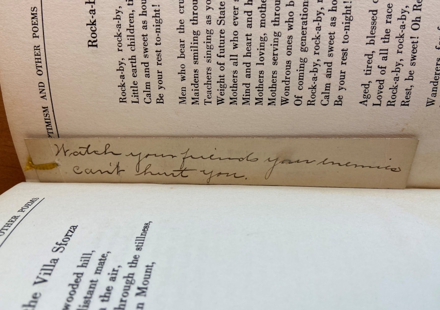 A thin bookmark with the remains of a frayed yellow tassel at one end is tucked in between two pages of the open book. In handwritten cursive it reads: "Watch your friends your enemies can't hurt you."